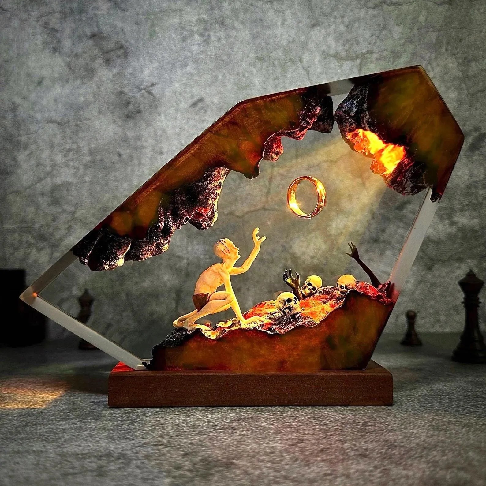Angled view of gaunt figure reaching toward a ring in ember-lit resin with layered depth and ember red, violet, and blue light
