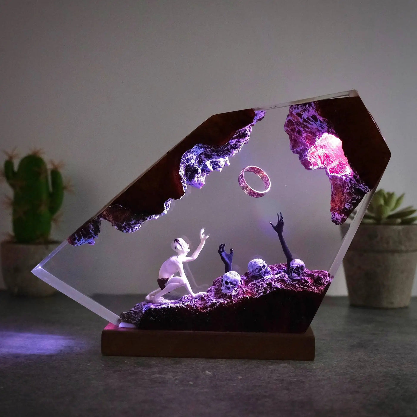 Close view of gaunt figure reaching toward a ring in ember-lit resin with hand-finished texture and ember red, violet, and blue light